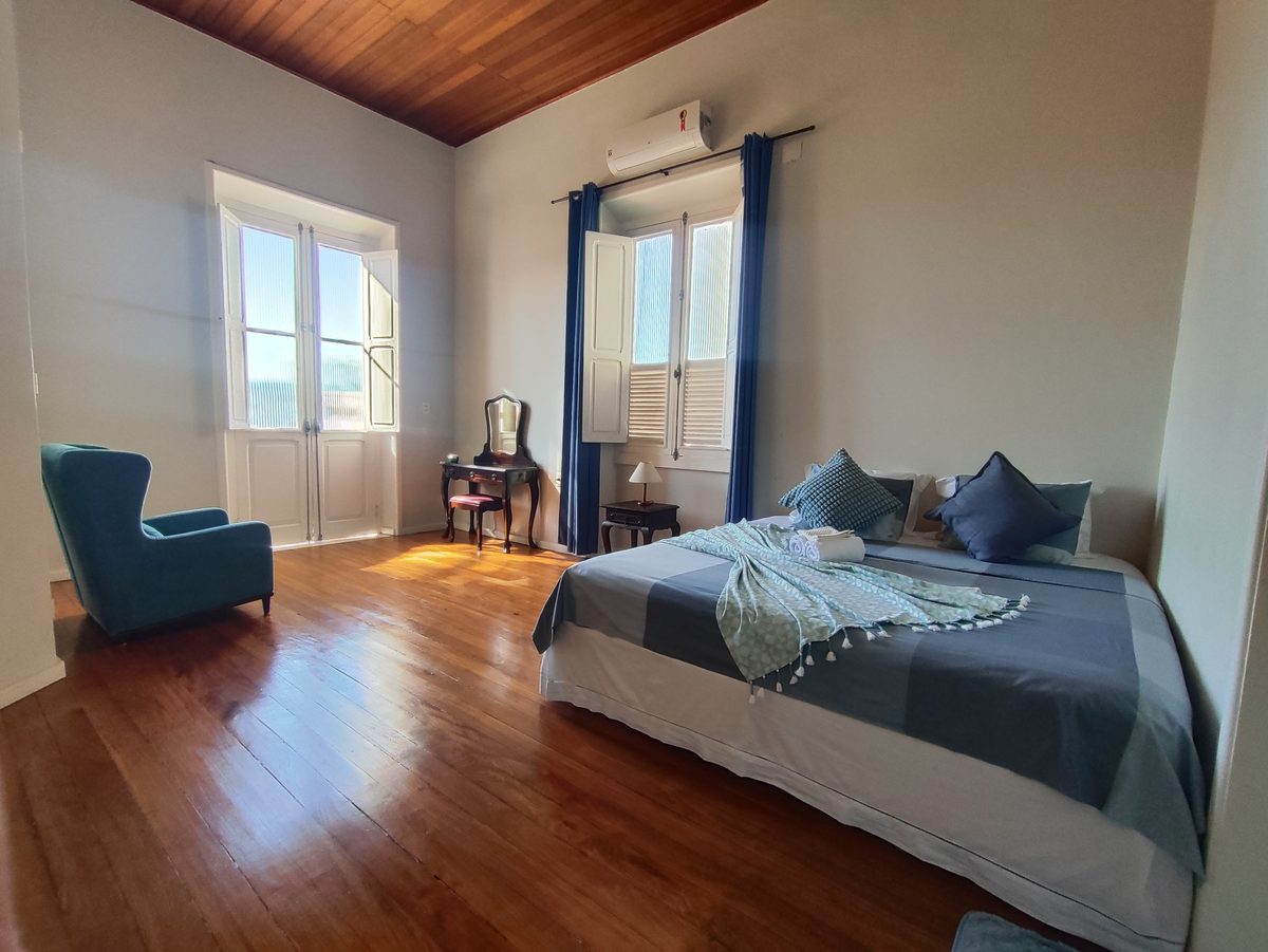 Suíte Tiê-Sangue da Villa Dourada com piso de madeira e janelas altas